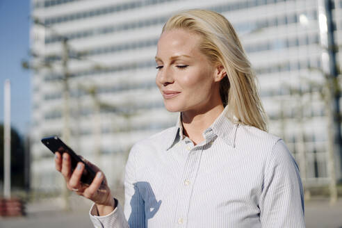 Schöne blonde Unternehmerin mit Smartphone in der Stadt an einem sonnigen Tag - JOSEF01026