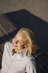 Smiling blond female entrepreneur soaking sunlight in city - JOSEF01031