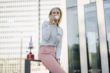 Blonde Geschäftsfrau trinkt Kaffee vor einem Gebäude im Finanzviertel - JOSEF01049