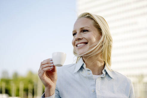 Lächelnde blonde Frau, die eine Kaffeetasse hält und in den Himmel schaut - JOSEF01050