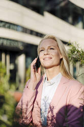 Lächelnde weibliche Fachkraft, die mit dem Handy telefoniert und dabei wegschaut, an einem sonnigen Tag - JOSEF01059