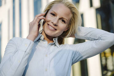 Close-up of beautiful smiling businesswoman talking on mobile phone at financial district in city - JOSEF01067