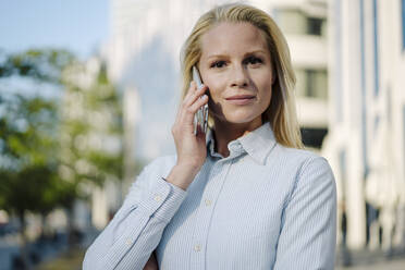 Selbstbewusste blonde Frau, die mit einem Mobiltelefon spricht - JOSEF01068