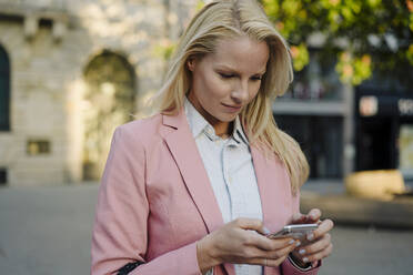 Schöne blonde Frau, die ein Smartphone im Finanzviertel der Stadt benutzt - JOSEF01089