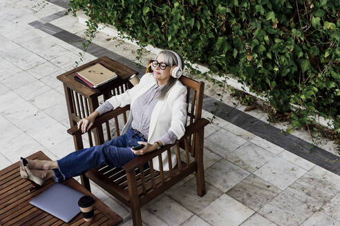 Ältere weibliche Fachkraft hört Musik und entspannt sich auf einem Stuhl im Garten - ERRF04083