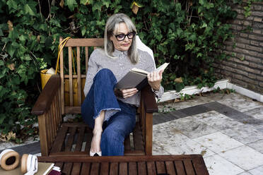 Ältere Unternehmerin macht Pause beim Lesen eines Buches im Garten - ERRF04093