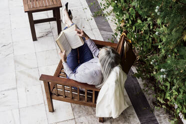 Relaxed businesswoman reading book while sitting on chair by plants at garden - ERRF04095
