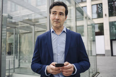 Thoughtful mature businessman with smartphone in the city - JOSEF01128