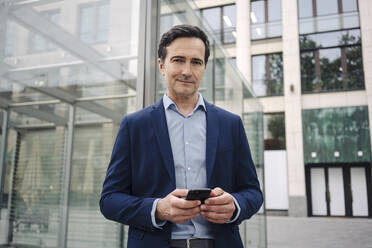 Portrait of a confident mature businessman with smartphone in the city - JOSEF01131