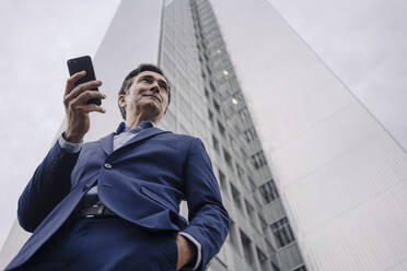 Älterer Geschäftsmann mit Smartphone vor einem Büroturm in der Stadt - JOSEF01147