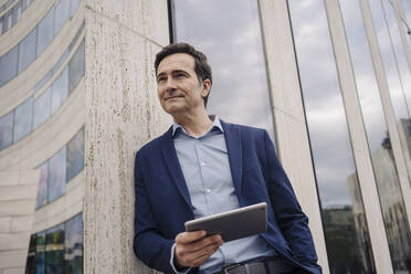 Mature businessman with tablet leaning against a building in the city - JOSEF01155