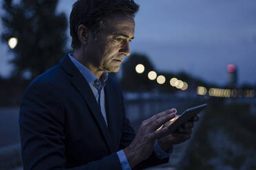 Älterer Geschäftsmann mit Tablet auf einer Promenade in der Abenddämmerung - JOSEF01171