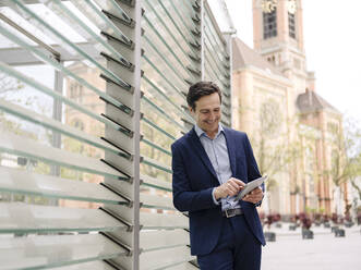 Smiling mature businessman using tablet in the city - JOSEF01184