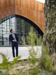 Mature businessman holding tablet in the city looking up - JOSEF01195