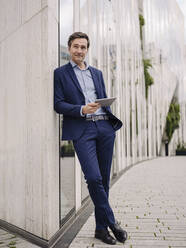 Mature businessman with tablet leaning against a building in the city - JOSEF01215