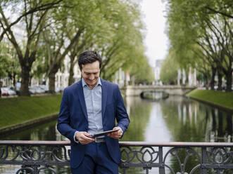 Mature businessman standing on a bridge using tablet - JOSEF01230