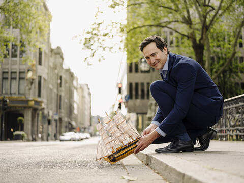 Lächelnder reifer Geschäftsmann, der ein Modell eines Segelschiffs auf die Straße stellt, lizenzfreies Stockfoto