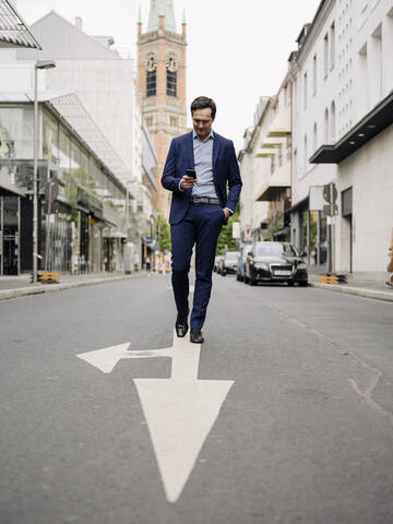 Älterer Geschäftsmann, der auf einer Straße in der Stadt spazieren geht und ein Smartphone benutzt, lizenzfreies Stockfoto