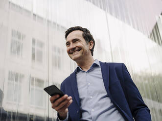 Happy mature businessman with smartphone in the city - JOSEF01256