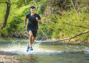 Junger männlicher Sportler beim Laufen und Spritzen von Wasser im Bach - STSF02553