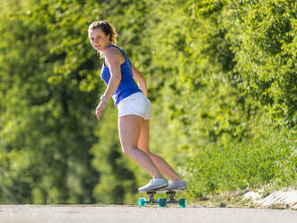 Junge Frau Skateboarding auf der Straße von Pflanzen während sonnigen Tag - STSF02555