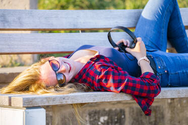 Smiling beautiful young woman lying on bench during sunny day - STSF02561