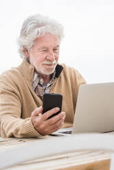 Senior man holding smart phone while using laptop at table - SIPF02175