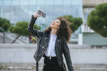 Cheerful young woman with afro hairstyle enjoying while dancing and listening music - KIJF03178