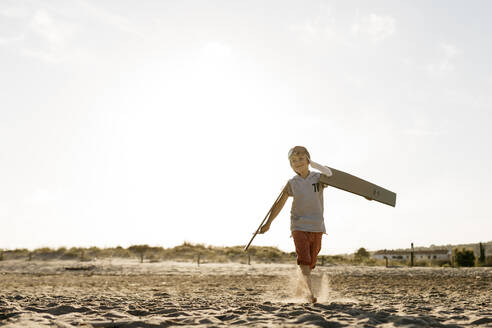 Junge mit Fliegermütze beim Laufen mit Pappflügeln am Strand - JRFF04559