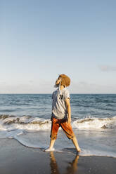 Boy wearing aviator's cap while standing at beach - JRFF04575