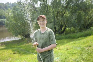 Smiling boy holding hose while standing in forest - VPIF02534