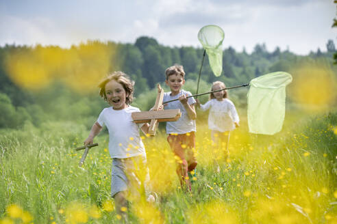 Carefree friends with model airplane and butterfly nets running on grassy land in forest - VPIF02536