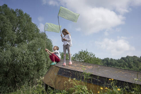 Friends catching butterflies with nets on abandoned boat against sky - VPIF02541