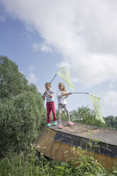 Freunde fangen Schmetterlinge mit Netzen, während sie auf einem verlassenen Boot gegen den Himmel stehen - VPIF02542