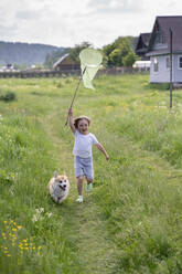 Playful boy holding butterfly net while running with dog on grassy land - VPIF02544
