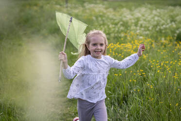 Smiling girl with butterfly net running on grassy land in forest - VPIF02546