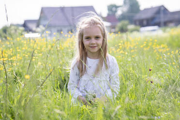 Smiling girl holding flowers sitting on grassy land - VPIF02549