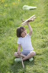 Playful boy flying model airplane while sitting on grassy land - VPIF02551