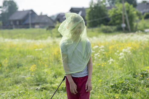 Playful boy wearing butterfly net while standing on grassy land - VPIF02552