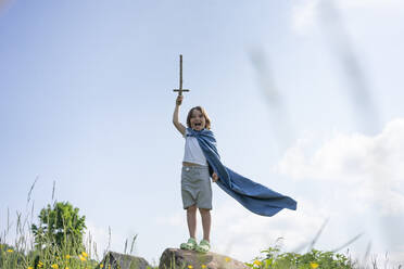 Boy wearing cape screaming while standing on rock against sky - VPIF02555