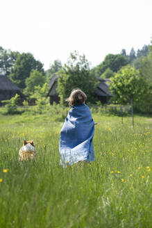 Boy wearing cape standing with dog on grassy land against clear sky - VPIF02557