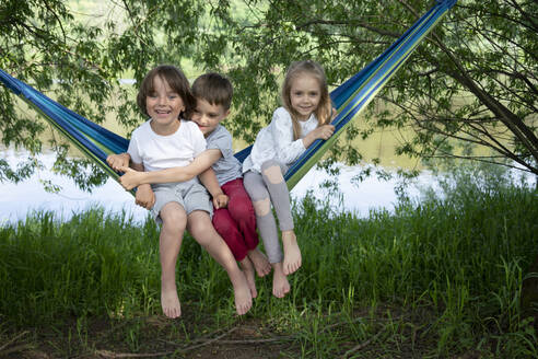Cheerful friends sitting on hammock in forest - VPIF02560