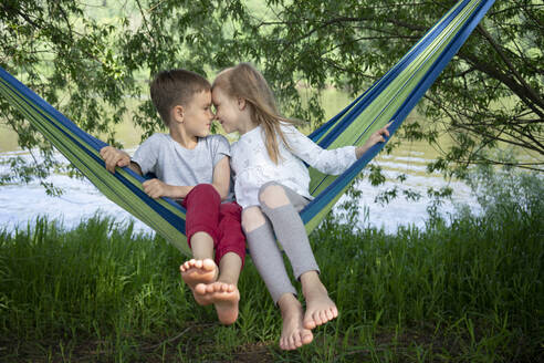 Cute friends with face to face sitting on hammock in forest - VPIF02564