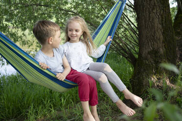Girl talking with boy while sitting on hammock in forest - VPIF02565