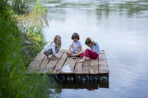 Happy children playing on pier over lake in forest - VPIF02569