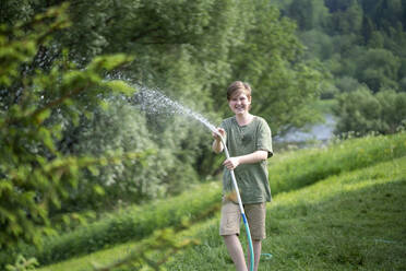 Lächelnder Junge, der mit einem Schlauch im Wald Wasser versprüht - VPIF02573