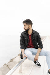 Thoughtful handsome man sitting on railing against clear sky - RDGF00001