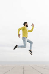 Carefree young man jumping on footpath against white wall - RDGF00002