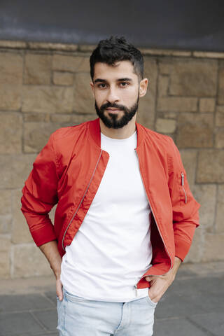 Handsome young man with hands in pockets standing against wall stock photo