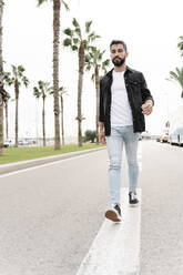 Young man walking on street against clear sky in city - RDGF00011